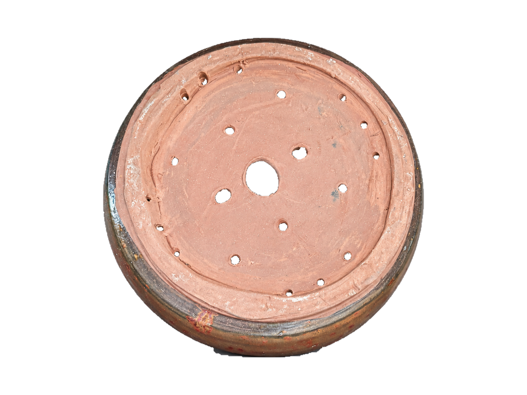 Underside of the bronze and copper pot showing the foot ring and irregular drainage and wiring holes