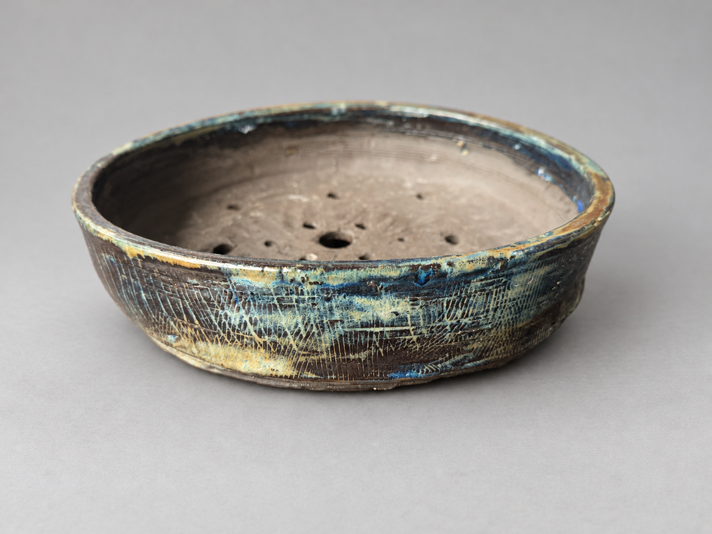 Front view of a handmade charcoal round ceramic pot with blue, teal and cream textured glaze