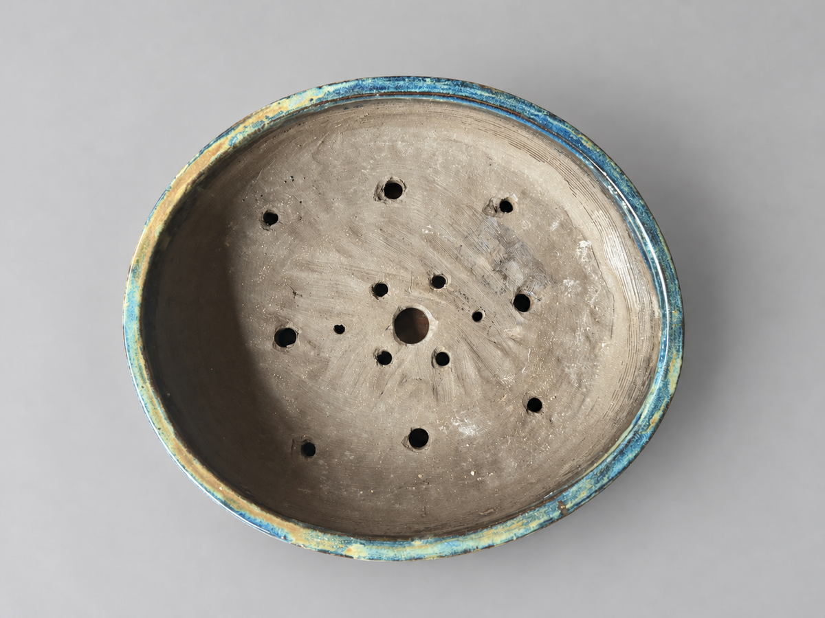 Top view of the blue and charcoal round pot showing its clay interior, drainage and wiring holes