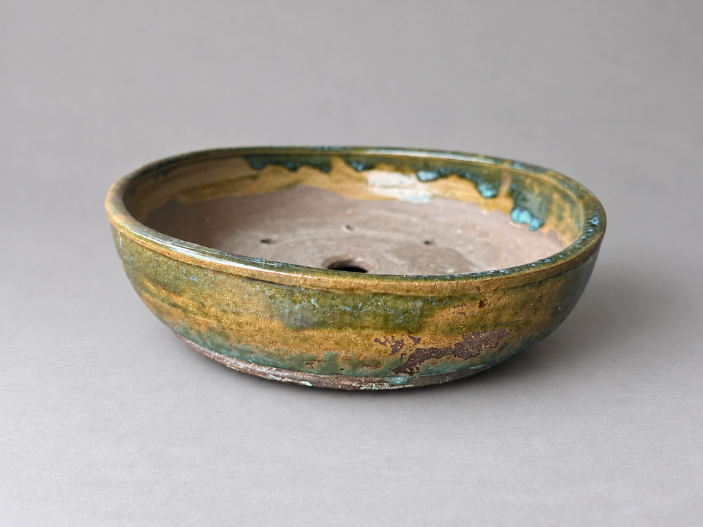 Front view of a handmade shallow round ceramic pot with amber and green glaze