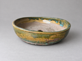 Front view of a handmade shallow round ceramic pot with amber and green glaze