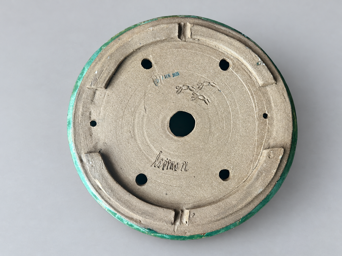 Underside of the amber and green round pot showing its foot ring, holes and maker marks