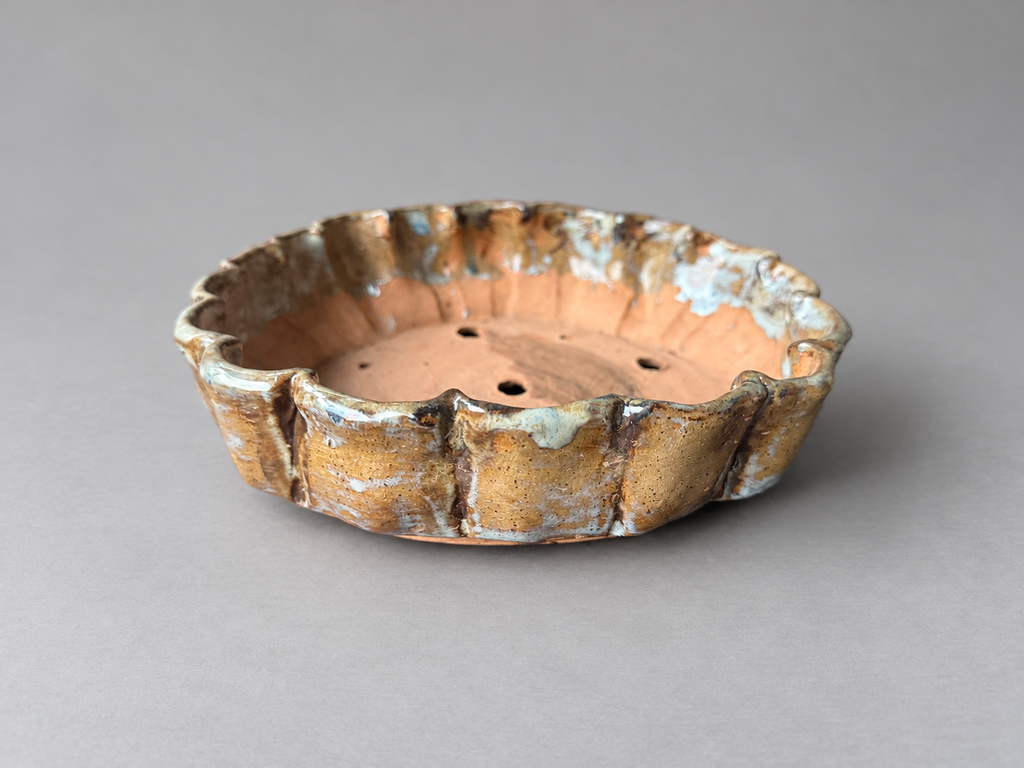 Front view of a handmade ochre and cream ceramic pot with a scalloped rim and folded vertical ridges