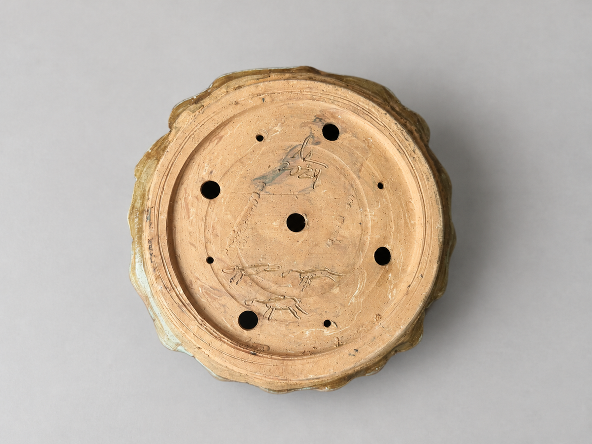 Underside of the scalloped pot showing its foot ring, holes and incised maker marks