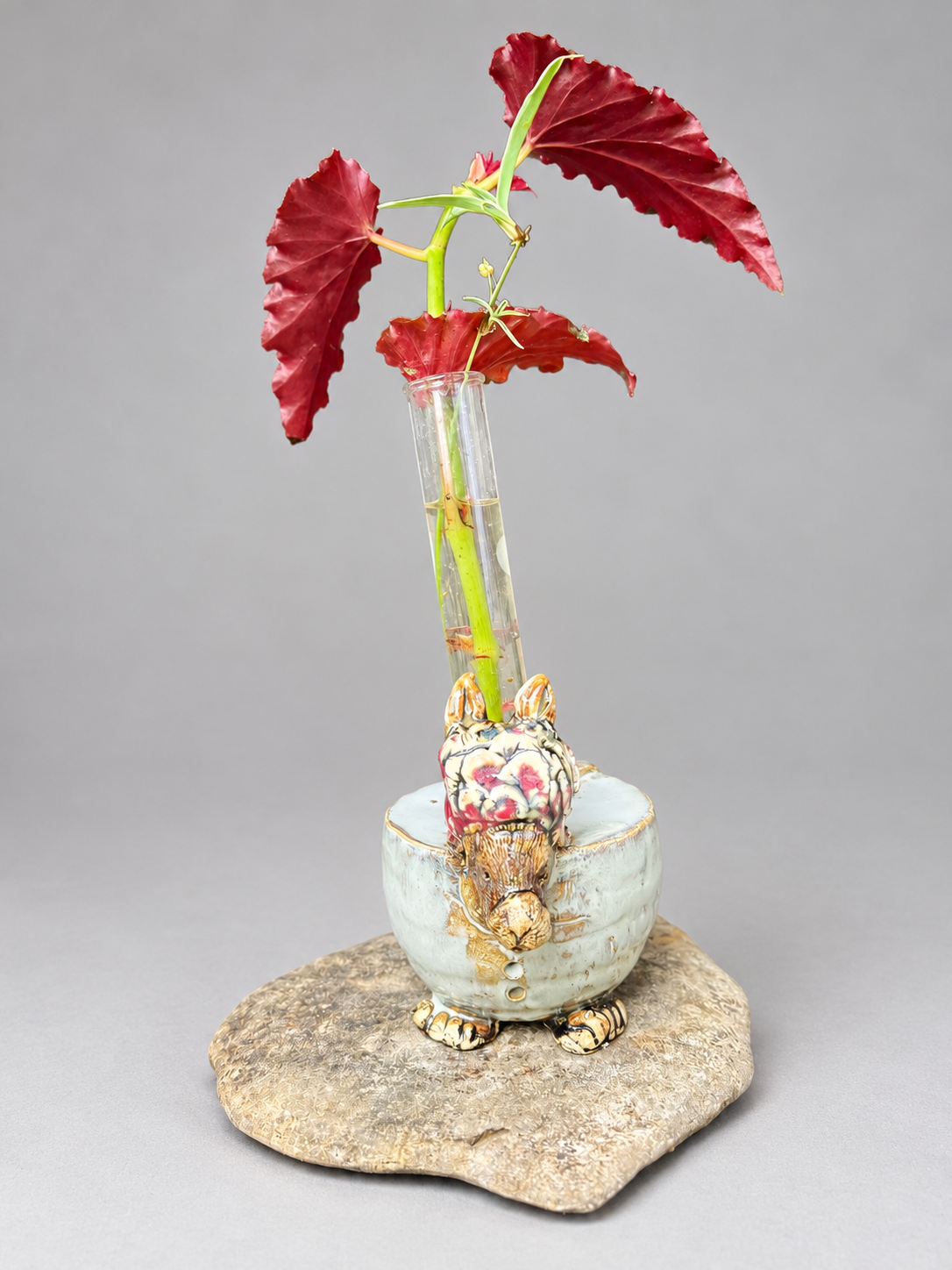 Decorated rabbit-shaped ceramic propagation stand displayed with a glass tube and a red-leaved plant cutting